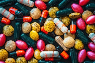 Many colorful (pink, black, white, orange, brown) antibiotic capsules and tablets piled together