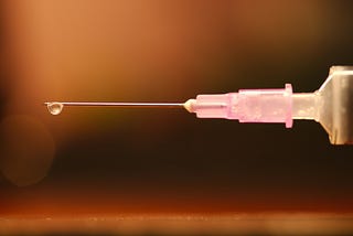 A syringe with a needle with a drop of fluid