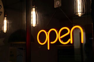 A yellow sign that says OPEN, against a dark background with some lightbulbs