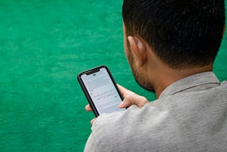 A young man looks at his phone in front of a green background