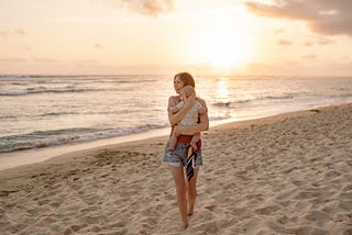 a mom walking on the beach while holding her baby