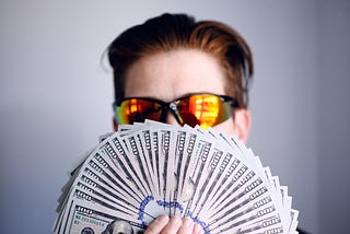 Guy in sunglasses, flashing a wad of $100 bills.