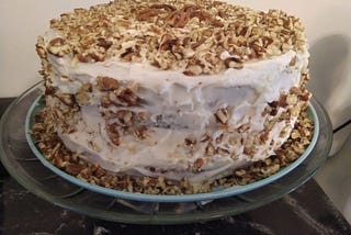 a 3-layered cake with white cream cheese icing, dusted with chopped pecans