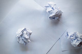 three crumpled pieces of paper on top of two blank sheets of paper
