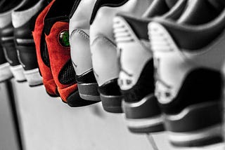 A black and white photo with sneakers on a shelf, one of them is red