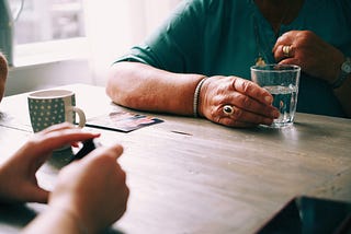 An older hand holding a cup of water across the table from a younger hand