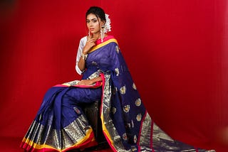 A woman wearing a navy blue saree background red color
