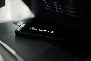 Phone lying on a laptop. Phone has OpenAI logo as the screensaver