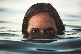 A woman’s head is visible in water up to her eyes.