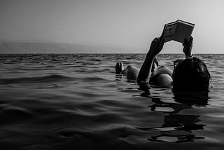 black and white photography, girl in the sea, holding a book, reading