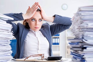 Overworked businesswoman with piles of papers surrounding her