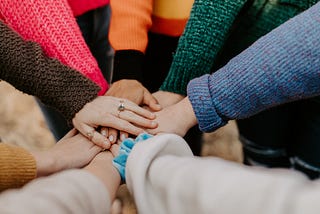 A group of people standing in a circle with their hands placed together in the center