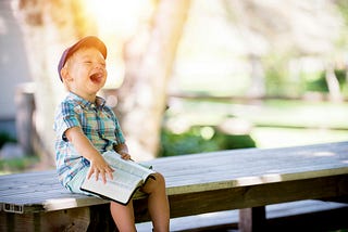 Young child lauging with an open book on his lap.