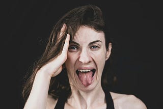 a woman with her hand in her hair by the side of her face, sticking out her tongue