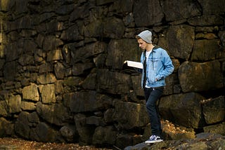 Man reading outdoors against stone wall backdrop