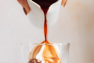 a cup of espresso being poured over vanilla ice cream that’s in a clear glass