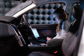 Woman looking at a laptop while her car automatically drives
