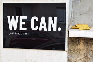 A black tile on a white wall with the words " we can. Just imagine" on it.