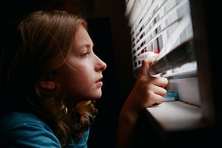 a nine year old girl looking out her window through the blinds