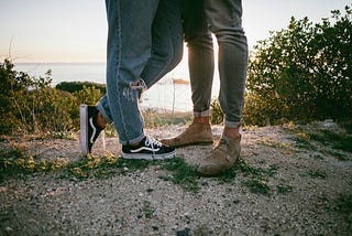 Two people in jeans from thigh down in green path down to water