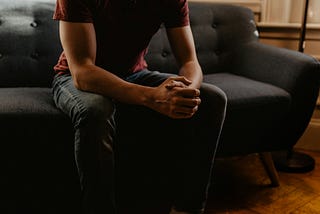 picture of a man from the neck down sitting in a listening position on a therapist couch