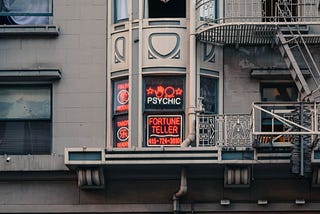 Picture of a window with a neon sign advertising for a psychic reader.