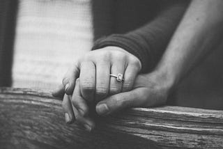 A pair of hands on a railing with a diamond ring on the woman’s hand.