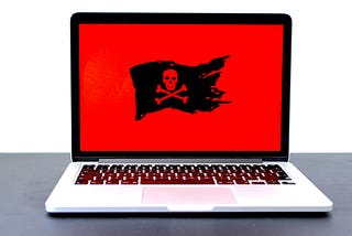 Laptop displaying a pirate flag / jolly roger on a red screen, possibly indicating malware, hackers or a different computer problem. If you like that image, consider donating at https://sharethemeal.org/donate - thanks!