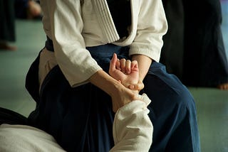 A photograph of a woman kneeling in a uniform, gripping another person’s wrist