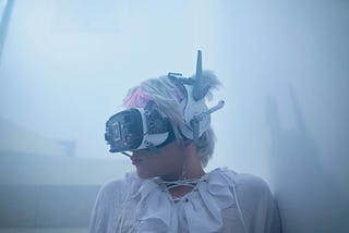 Head-and-shoulders of a person in white wearing a VR headset and earphones. Looks like a very retro white smock. Foggy background.