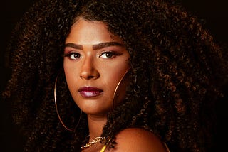Portrait of a young woman with curly hair wearing makeup and hoop earrings and looking into the camera
