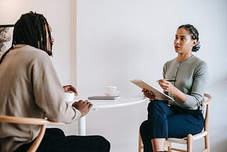 Two people sitting at the table, one person asking question to the other