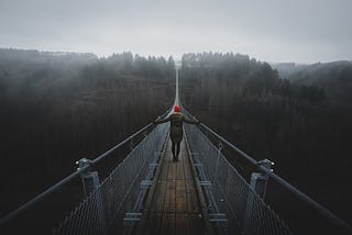 Woman with red beanie crossing a high bridge surrounded by haze