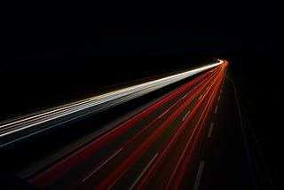 Lines of speeding light down a highway. Photo by Christian Englmeier on Unsplash.