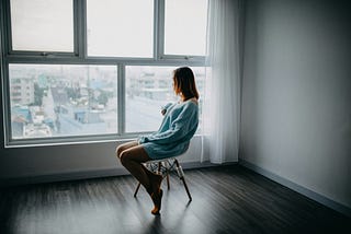 Woman sitting in a chair looking out a window at a city scene.