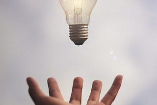 Hand reaching out to catch a lit lightbulb
