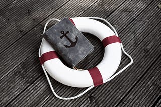 Bible with anchor laying in lifesaver on wooden planks. The Bible is an anchor in our time. And God’s word offers salvation for all people. This is the foundation of our life, 100% because of Yeshua, Jesus the Christ finished work.