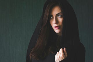 A woman with a cloak — we can see her face and hand. She appears to be frightened.