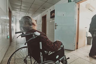 An elderly individual seated in a wheelchair, showing resilience and determination following a stroke.