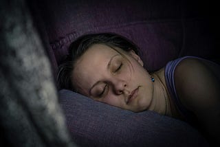 The photo shows a woman sleeping on her right side, her head on a pillow. The room is dark, indicating she is sleeping at night.