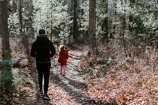 A father walking behind his daughter along a path in the woods