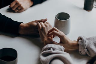 two people holding hands with two coffee cups on the table next to them