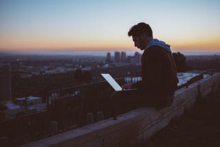 A man works at a laptop while sitting on a rooftop
