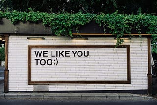 White wall with plants above with the text “we like you, too :)”