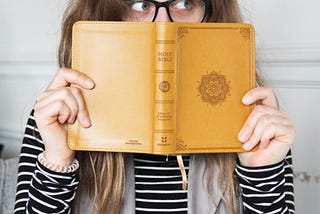 A young woman peers at something from behind a Bible.