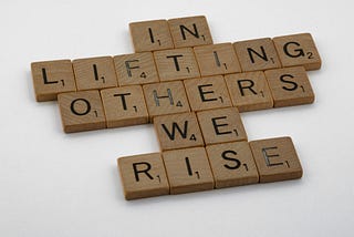 scrabble cubes spelling out “In lifting others we rise.”