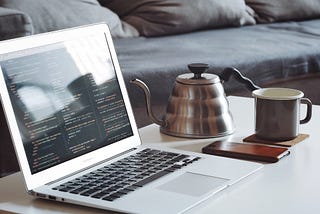 A laptop computer and a tea kettle resting on a table.