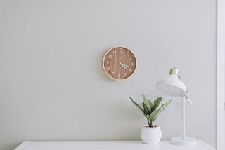 Wooden wall clock over a white desk and plant.