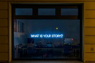 A window at night with ‘What is your story?’ written in lights.