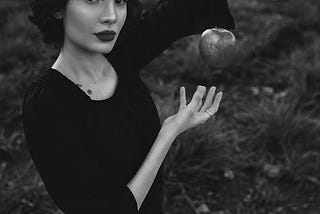 black and white photo of woman in black dress making an apple float in the air.